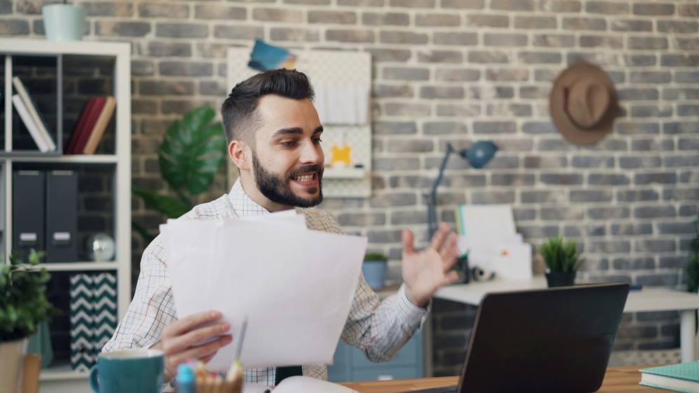 Unhappy businessman looking at laptop screen and throwing documents